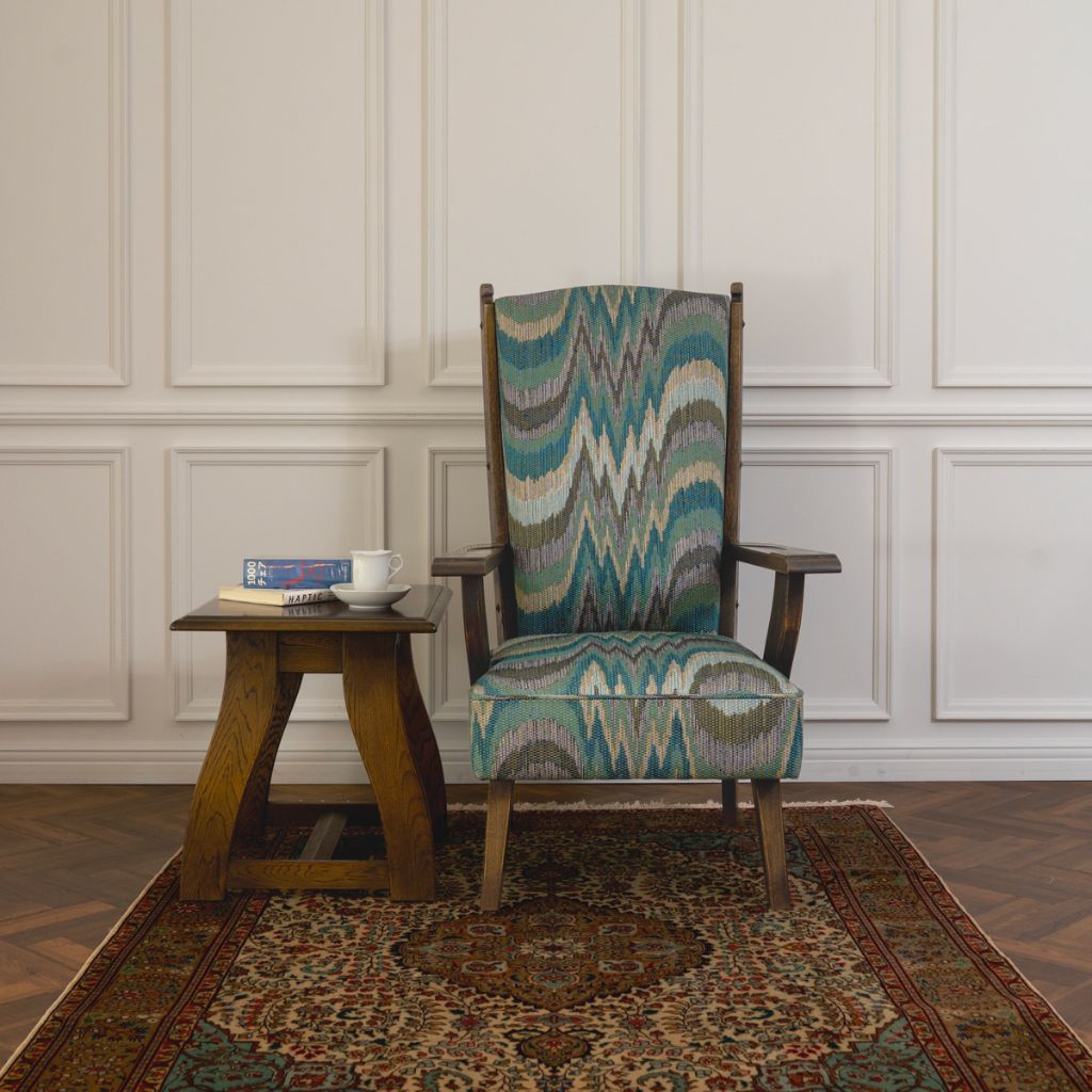 High-backed armchair upholstered in a patterned fabric, beside a small wooden side table