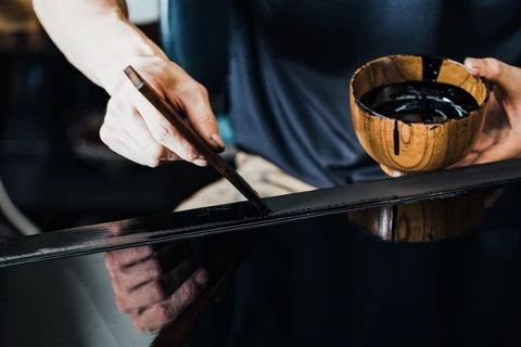 A craftsperson applying lacquer to a dark surface with a brush