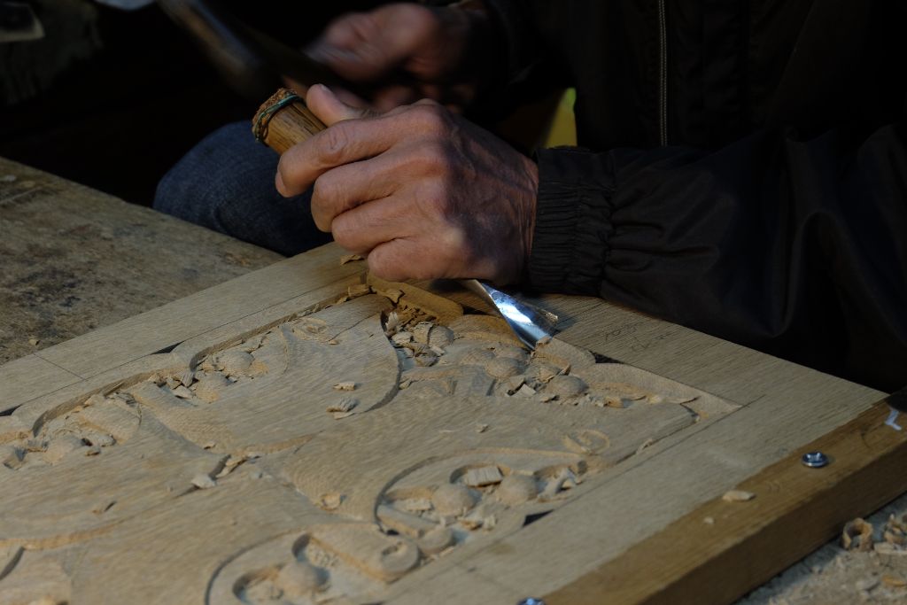 Hands carving an ornamental pattern into a wooden panel
